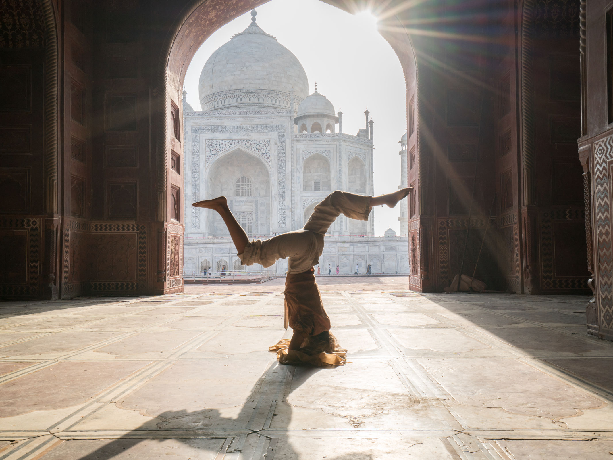 Young woman practicing yoga in India at the famous Taj Mahal at sunrise - Headstand position upside down.